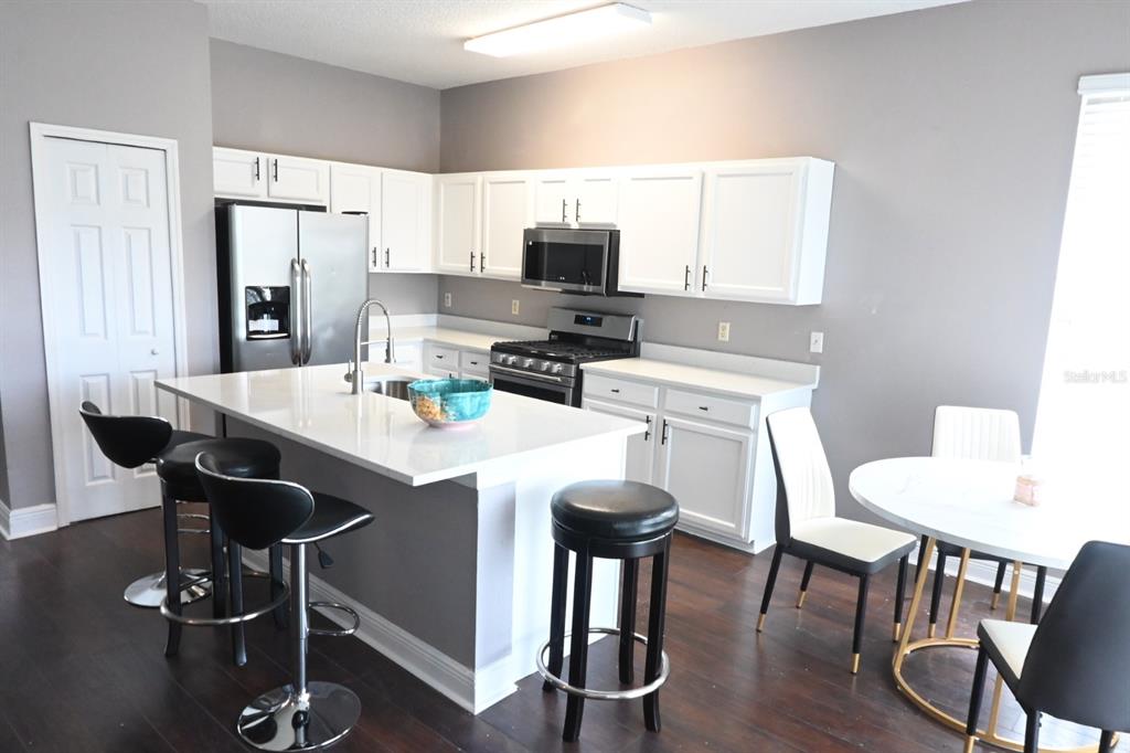 A kitchen features white cabinets, a central island with bar stools, and dark wood flooring — 919 JAYBEE AVENUE, DAVENPORT, FL