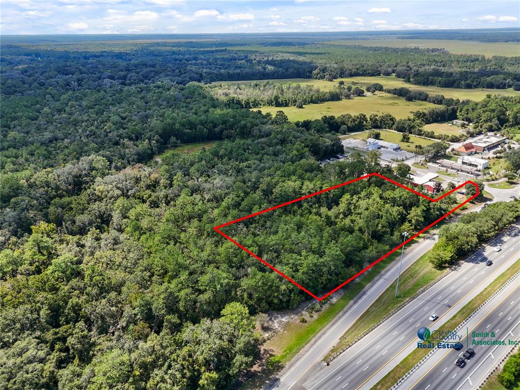 An aerial view shows a rectangular plot of wooded land adjacent to a multi-lane highway — SE CR 234, MICANOPY, FL