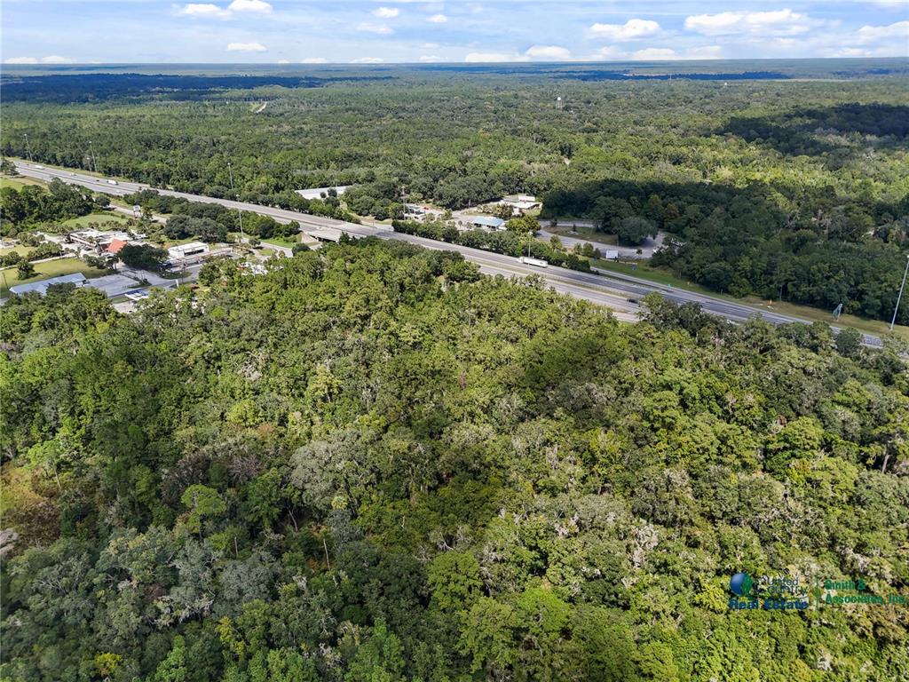 An aerial view shows a dense forest bordering a multi-lane highway and nearby commercial buildings — SE CR 234, MICANOPY, FL