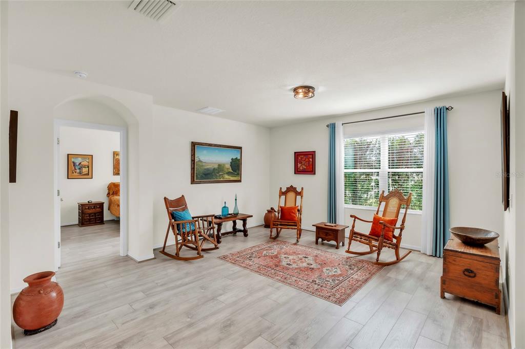 A living room features light wood-look flooring, three wooden rocking chairs, and a patterned area rug — 9527 SUNSTONE BOULEVARD, THONOTOSASSA, FL