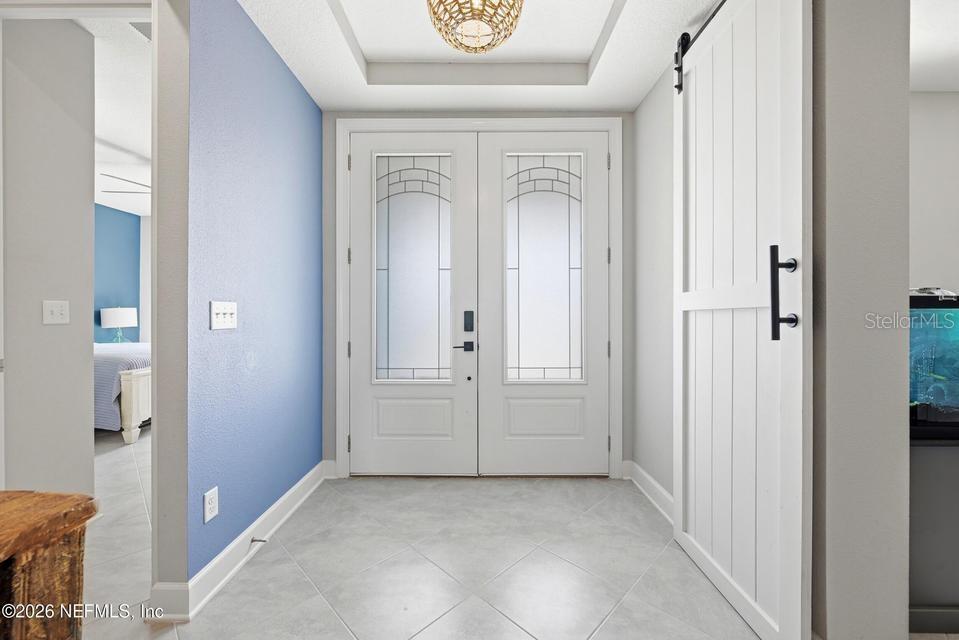 This entryway features a white double door, light tile flooring, and a sliding barn door — 128 WINDWALKER DRIVE, ST AUGUSTINE, FL