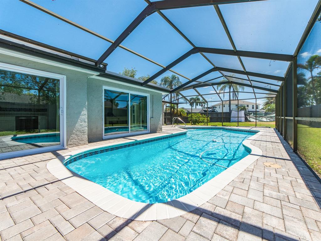 A screened-in swimming pool with a paver deck sits behind a house with sliding doors — 3645 OVERLAND, HOLIDAY, FL