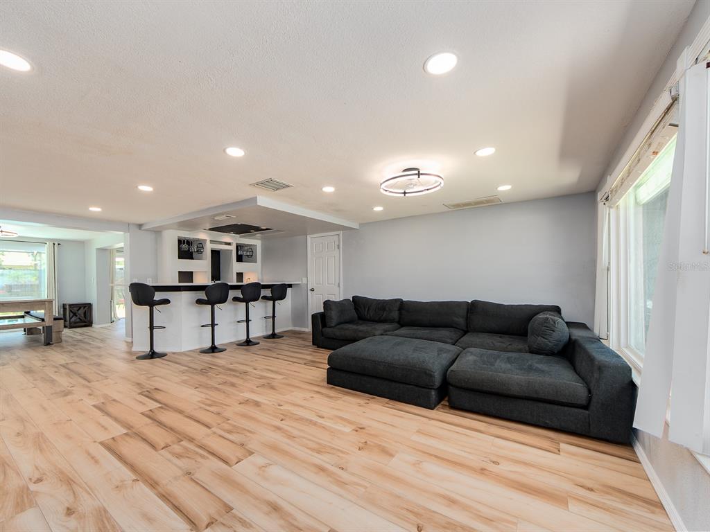 A living room features light wood-look flooring, a large dark sectional sofa, and a wet bar — 3645 OVERLAND, HOLIDAY, FL