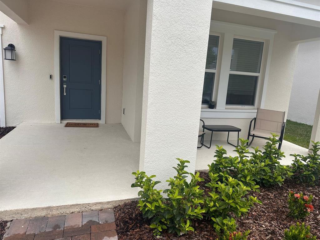 A covered front porch features a blue door, a window, and a small seating area — 4205 JESPERSEN STREET, APOPKA, FL
