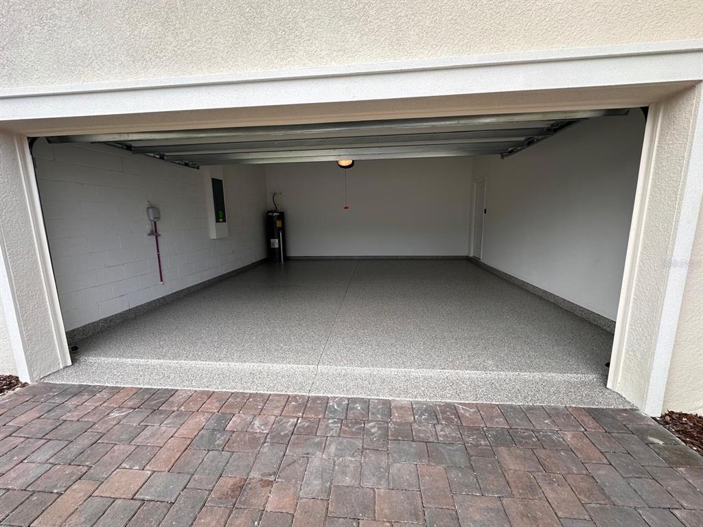 An open garage with a speckled epoxy floor, white walls, and a water heater — 4205 JESPERSEN STREET, APOPKA, FL