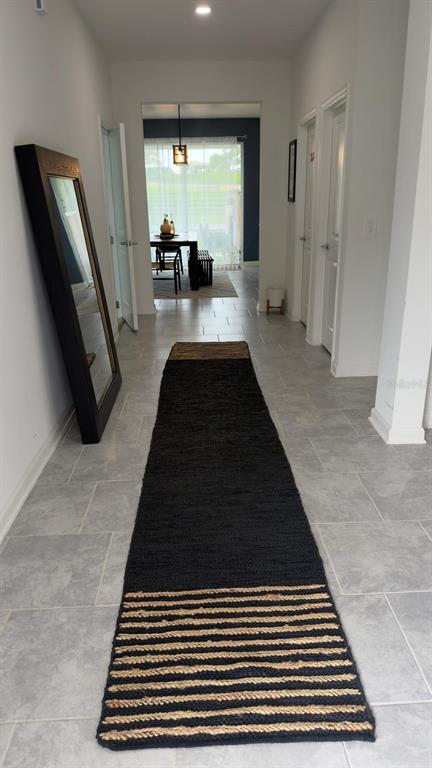 A long hallway with light tile flooring features a black runner rug and a floor mirror — 4205 JESPERSEN STREET, APOPKA, FL