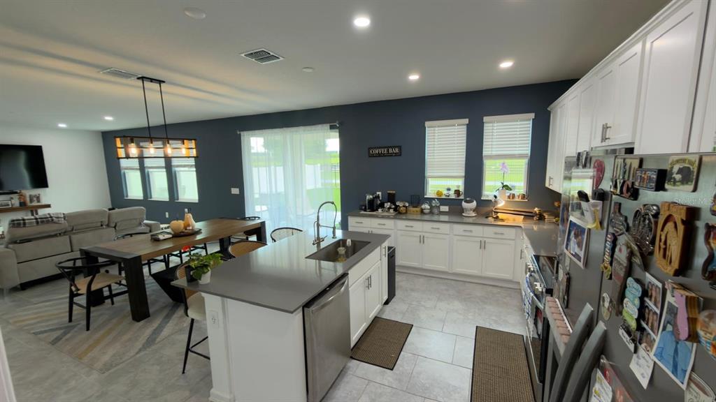 An open-concept kitchen features white cabinets, gray countertops, a center island, and a dining area — 4205 JESPERSEN STREET, APOPKA, FL