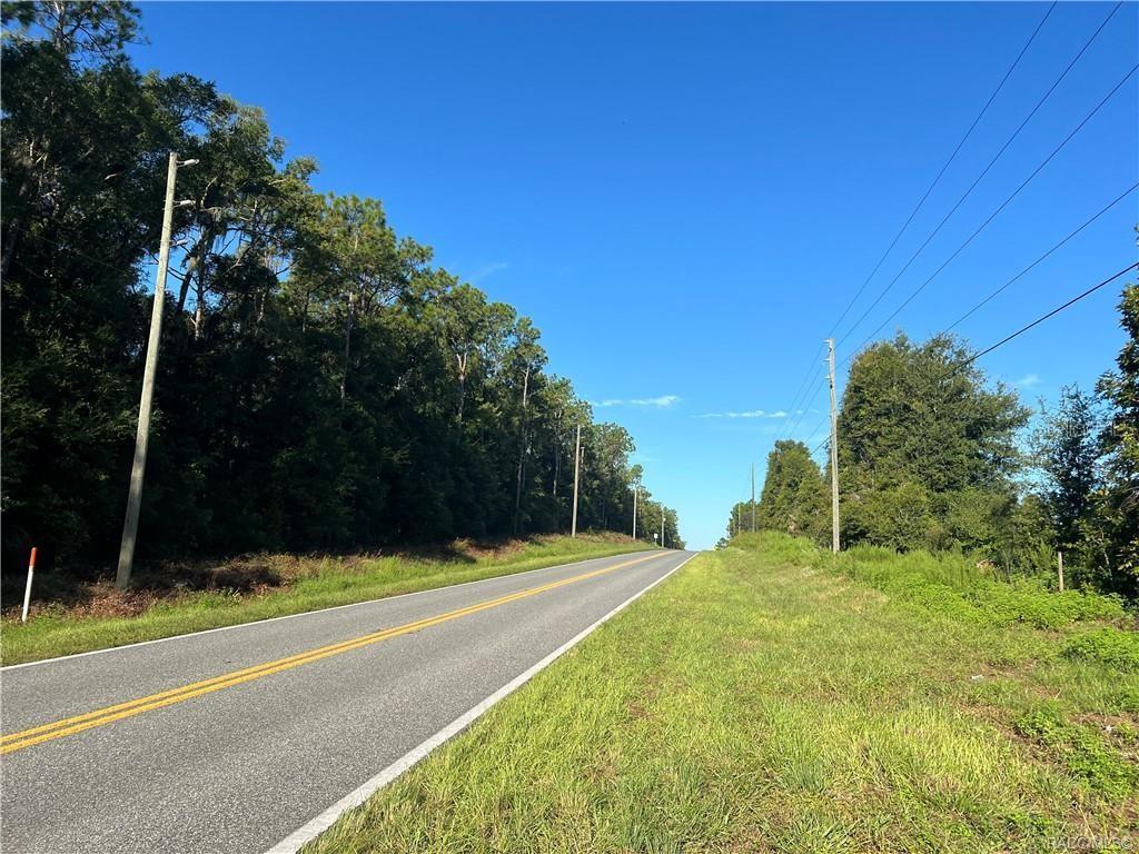 A paved road stretches into the distance, flanked by trees and utility poles under a sky — 3261 E STAGE COACH TRAIL, INVERNESS, FL