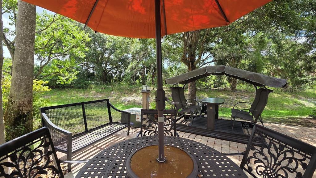 A patio features a metal dining set, a bench, and a covered swing under trees — 171 APPALOOSA TRAIL, RIVER RANCH, FL