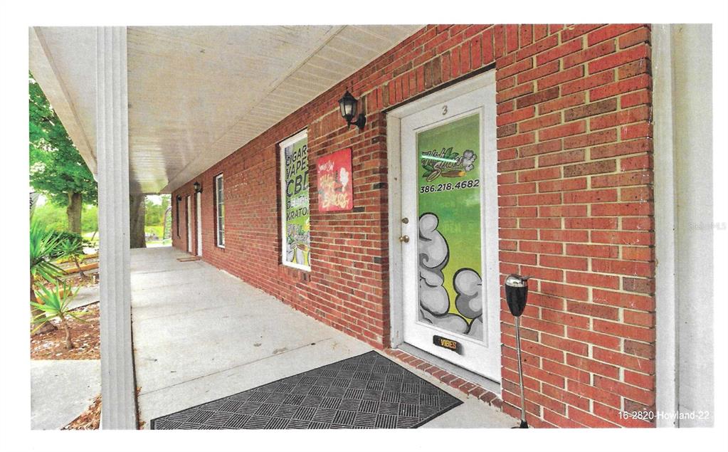 A brick building exterior features a covered walkway, a glass door, and a storefront sign — 2820 HOWLAND BOULEVARD, DELTONA, FL