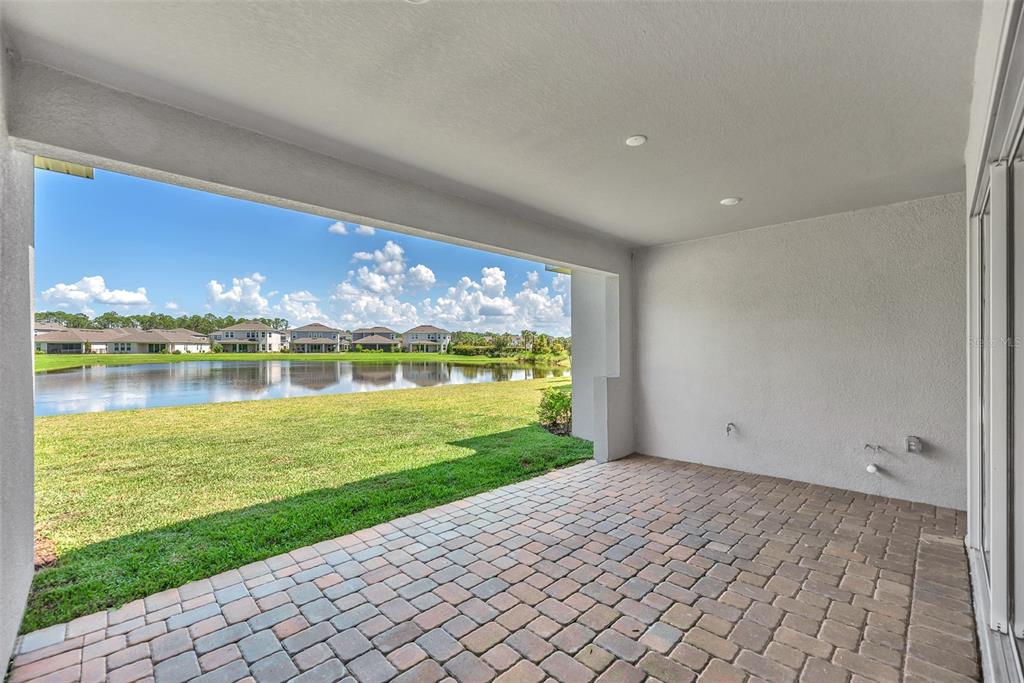A covered patio with brick pavers overlooks a grassy lawn and a pond — 33372 LANDSMAN LOOP, WESLEY CHAPEL, FL