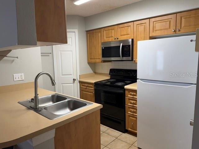 A kitchen features light wood cabinets, a black stove, a white refrigerator, and a double sink — 1000 W HORATIO STREET UNIT 226, TAMPA, FL