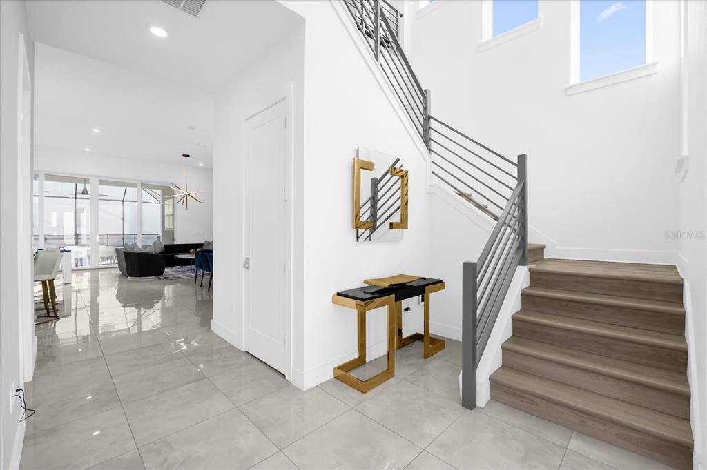 A bright entryway features a modern staircase, gold accent furniture, and light-colored tile flooring — 2137 PINE OAK LOOP, DAVENPORT, FL