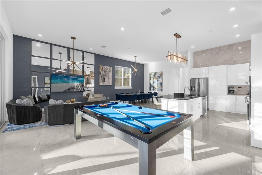 A modern open-concept living area features a pool table, kitchen, and dining space with tile floors — 2137 PINE OAK LOOP, DAVENPORT, FL