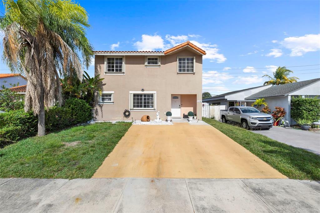 A two-story house with a tan stucco exterior, a paved driveway, and a palm tree — 11951 SW 208TH TERRACE, MIAMI, FL
