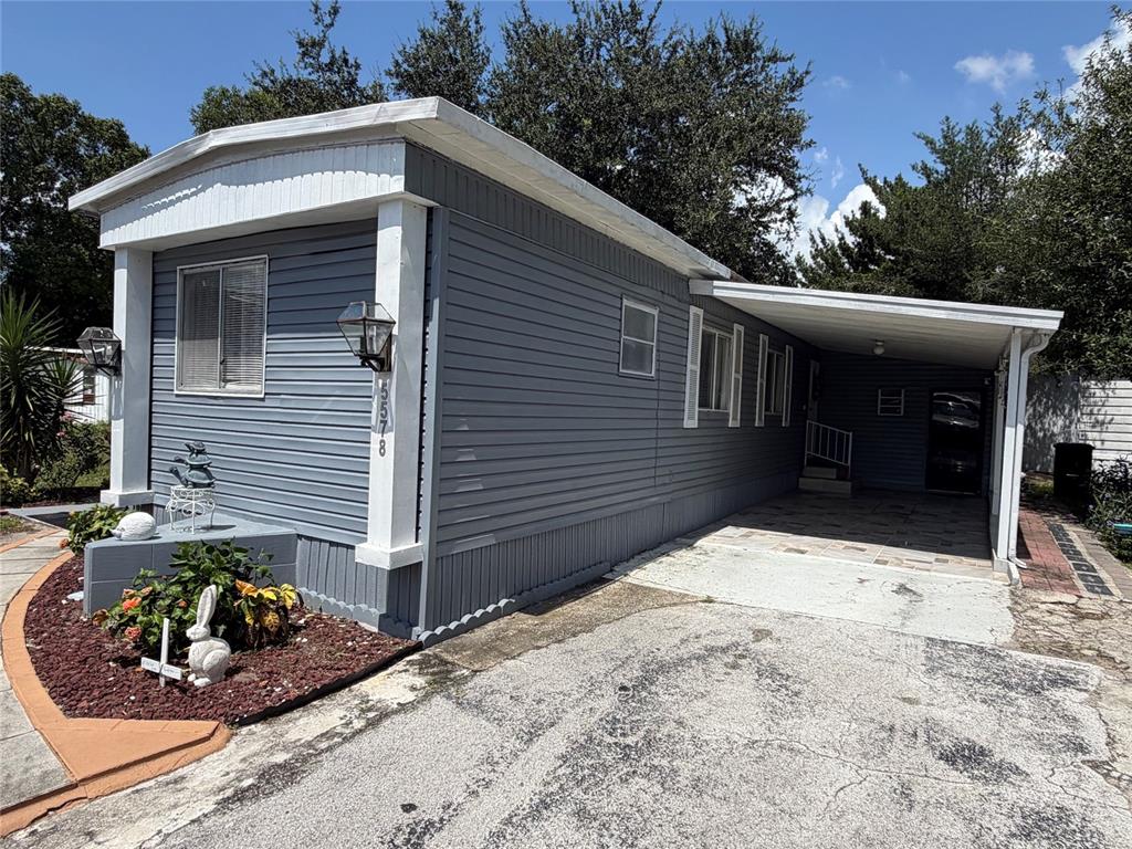 A gray mobile home features a side carport, a small front garden, and white trim — 5578 DENISE AVE, ORLANDO, FL