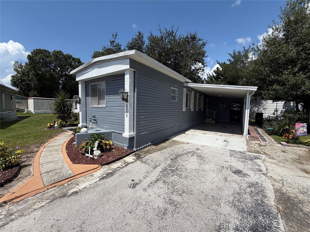A grey mobile home with a carport and a paved walkway sits on a grassy lot — 5578 DENISE AVE, ORLANDO, FL