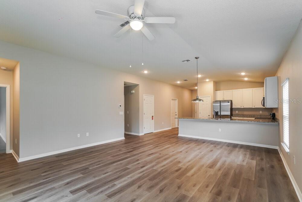 An open-concept living room features light-colored walls, wood-look flooring, and a kitchen with white cabinets — 722 FULMAR COURT, POINCIANA, FL