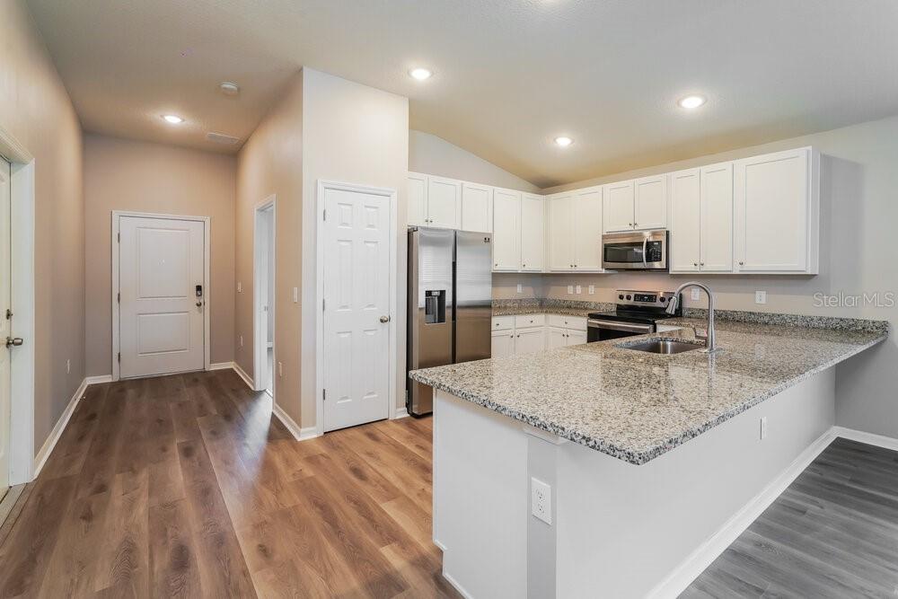 A kitchen with white cabinets, granite countertops, and stainless steel appliances opens to a hallway — 722 FULMAR COURT, POINCIANA, FL
