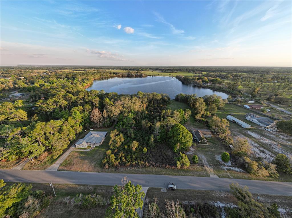 An aerial view shows a house, a wooded lot, and a lake under a blue sky — #8 MITCHEL WAY, EUSTIS, FL