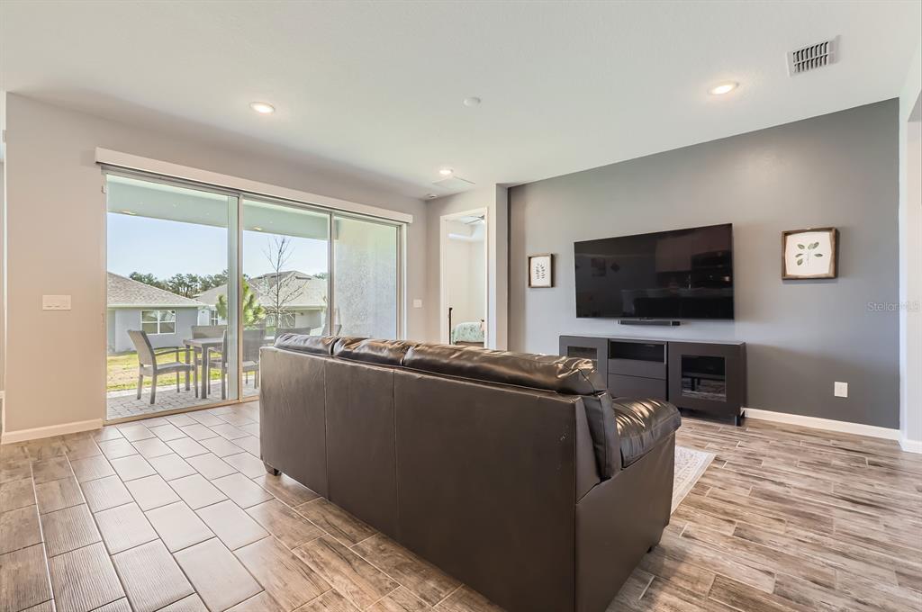 An open-concept living room with tile flooring, a black leather sofa, and sliding glass doors — 2372 SIRENA LANE, MOUNT DORA, FL