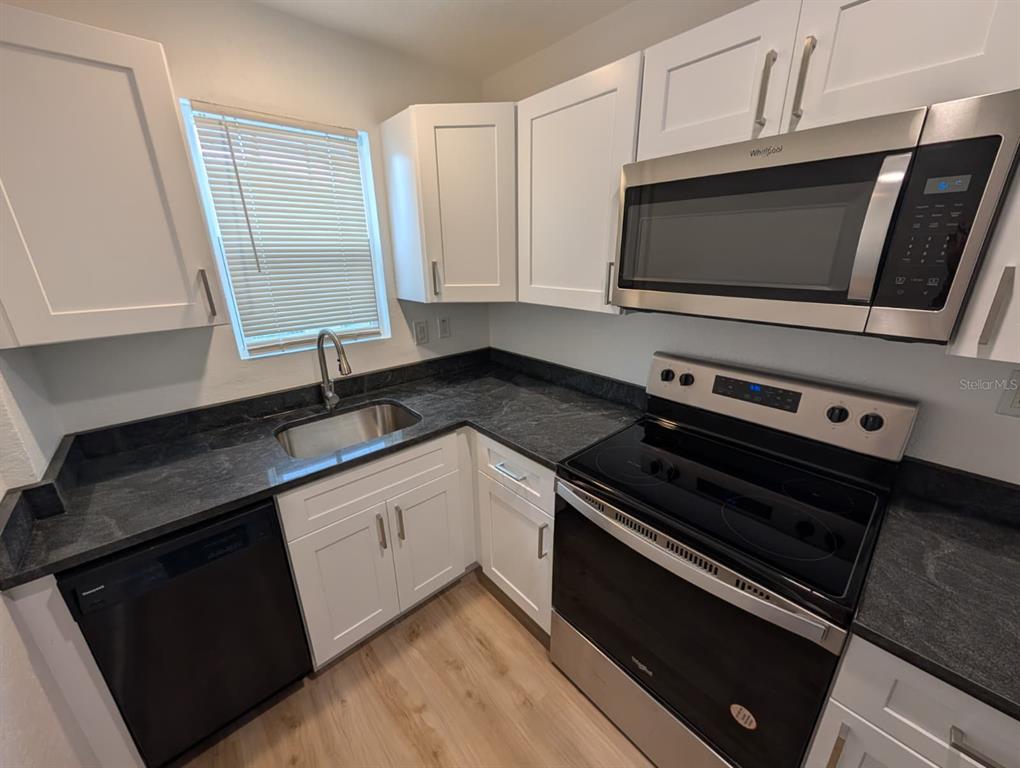 A kitchen features white cabinets, stainless steel appliances, a black refrigerator, and light wood flooring — 1834 28TH AVENUE N, ST PETERSBURG, FL