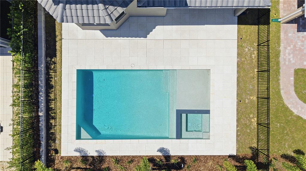 An aerial view shows a rectangular swimming pool with an integrated spa and light-colored pavers — 16114 VOLTERRA POINT, BELLA COLLINA, FL