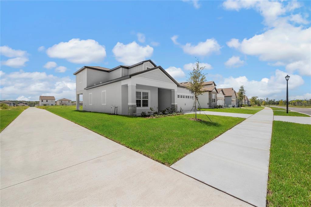 A light gray, two-story suburban house with a concrete driveway and sidewalk under a blue sky — 3348 CHINOTTO DRIVE, LAKE ALFRED, FL