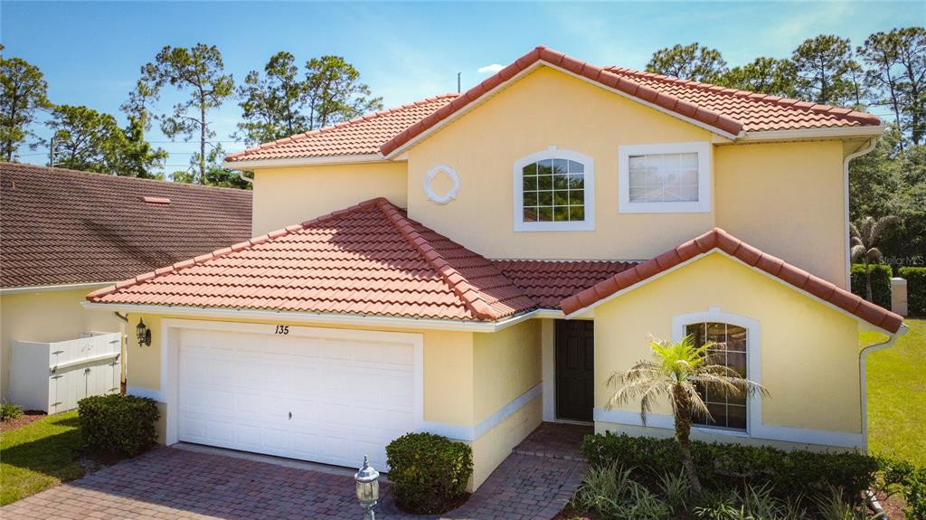 A two-story yellow house features a red tile roof, a white garage, and a palm tree — 135 ROBIN ROAD, DAVENPORT, FL