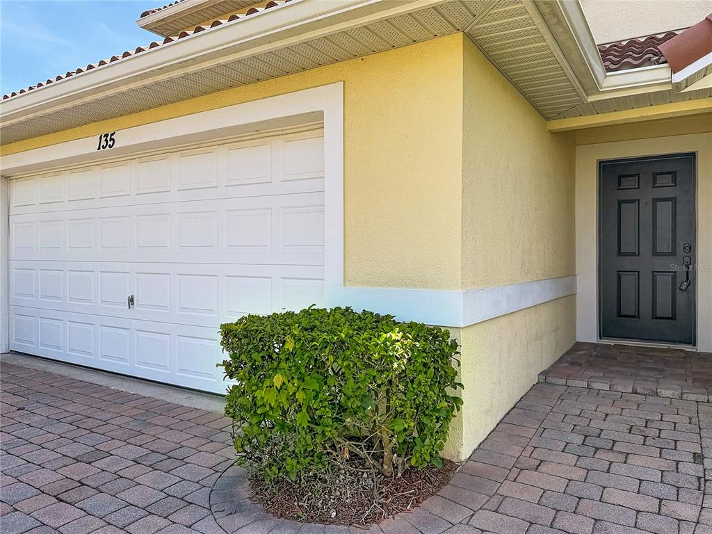 A yellow house exterior features a white garage door, a dark front door, and landscaping — 135 ROBIN ROAD, DAVENPORT, FL