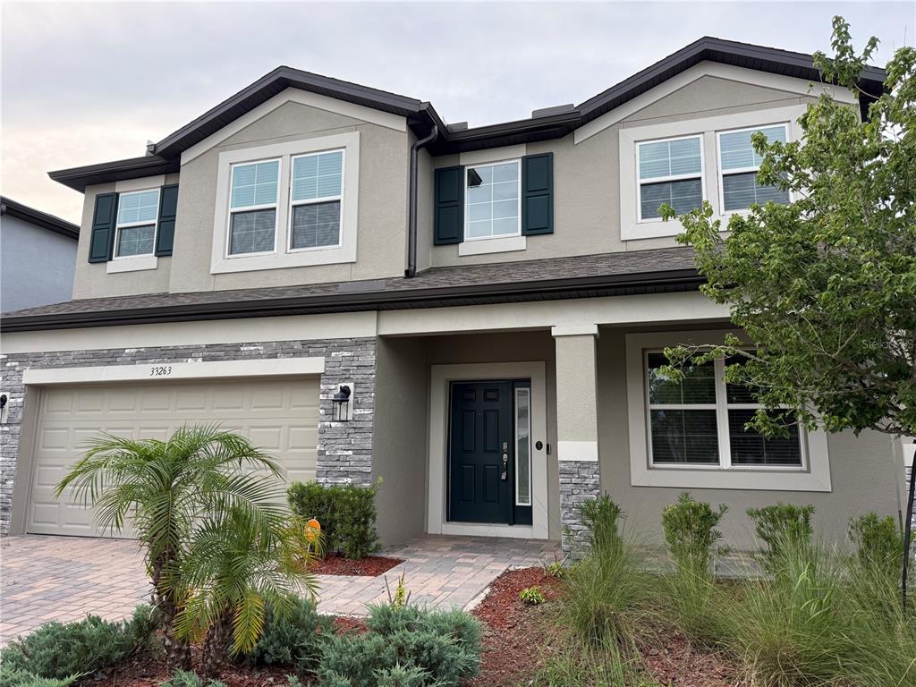 A two-story house features a stone-accented facade, a two-car garage, and a dark front door — 33263 SYCAMORE LEAF DRIVE, WESLEY CHAPEL, FL