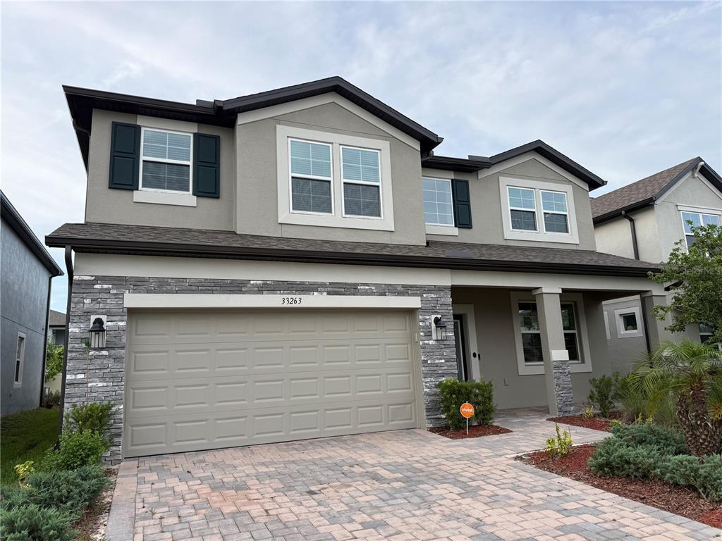 A two-story house features a stone-accented facade, a two-car garage, and a paved driveway — 33263 SYCAMORE LEAF DRIVE, WESLEY CHAPEL, FL