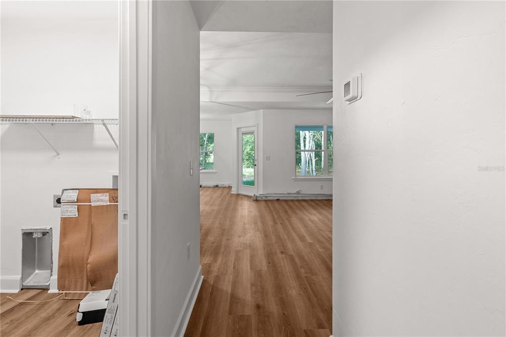 A hallway features wood-look flooring, white walls, and a door leading to a bright room — 7970 NE 102ND COURT, BRONSON, FL
