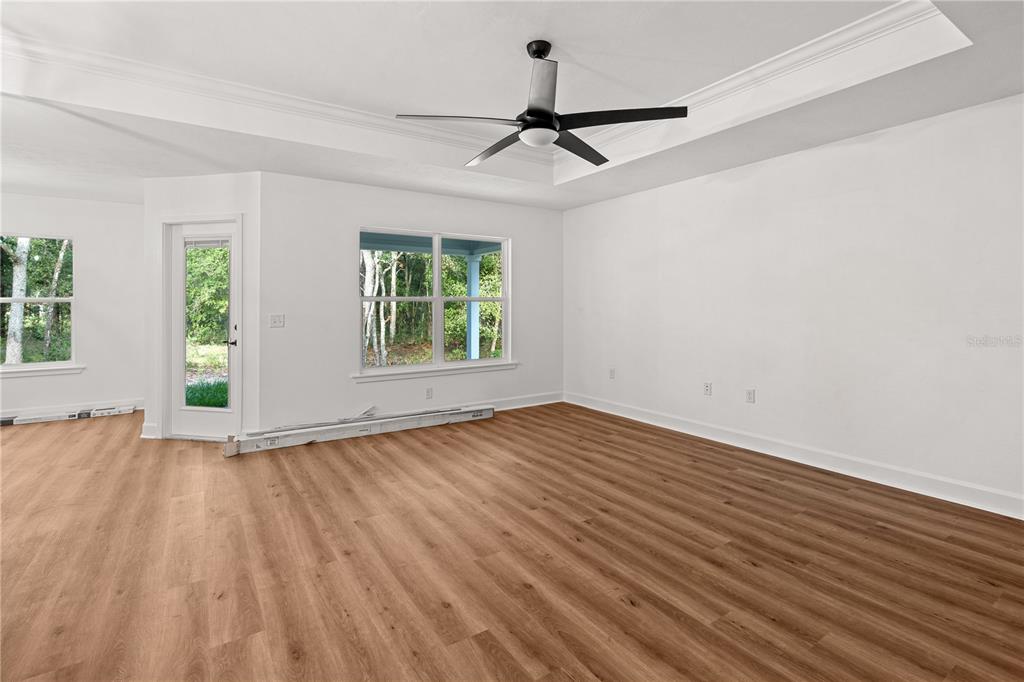 An open-concept living area features wood-look flooring, a tray ceiling with a fan, and windows — 7970 NE 102ND COURT, BRONSON, FL