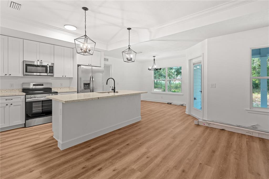 A kitchen features white cabinets, granite countertops, a center island, and wood-look flooring — 7970 NE 102ND COURT, BRONSON, FL