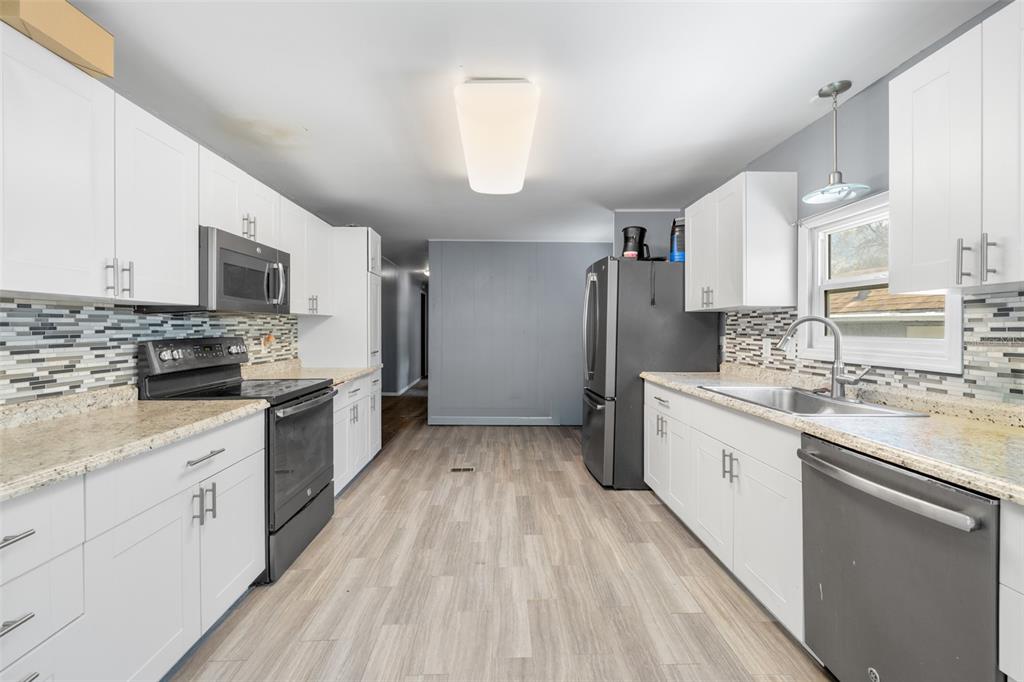 A galley kitchen features white cabinets, granite countertops, a mosaic backsplash, and stainless steel appliances — 3822 ALICE DRIVE, WESLEY CHAPEL, FL