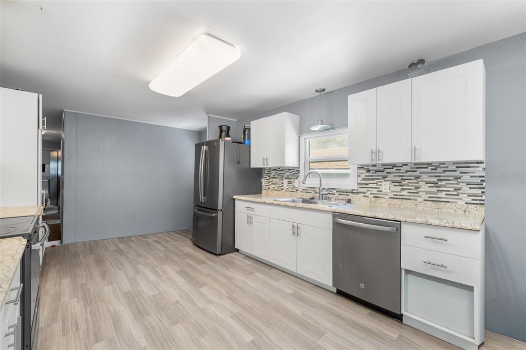 A kitchen features white cabinets, stainless steel appliances, a tiled backsplash, and light wood flooring — 3822 ALICE DRIVE, WESLEY CHAPEL, FL