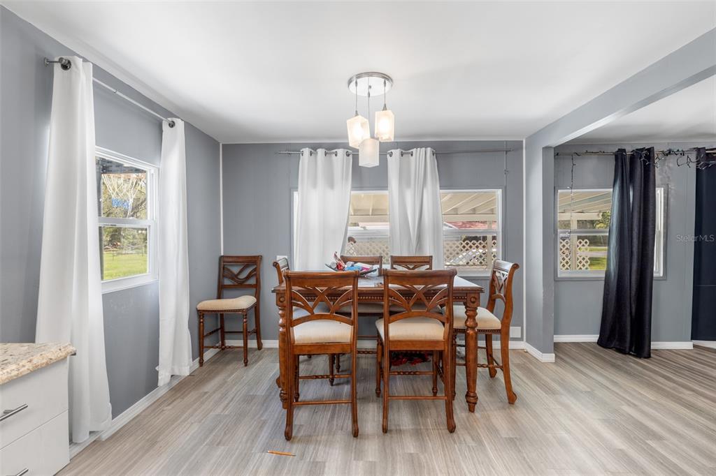 A dining room features gray walls, wood-look flooring, a wooden table with chairs, and white curtains — 3822 ALICE DRIVE, WESLEY CHAPEL, FL