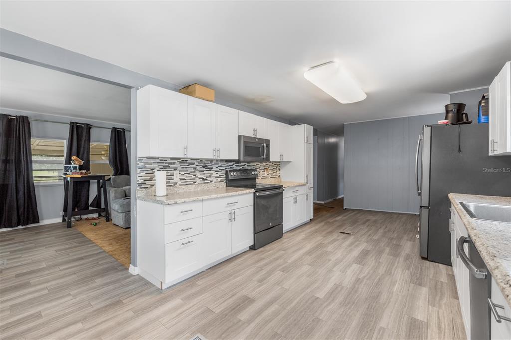 A kitchen with white cabinets, granite countertops, and stainless steel appliances features wood-look flooring — 3822 ALICE DRIVE, WESLEY CHAPEL, FL