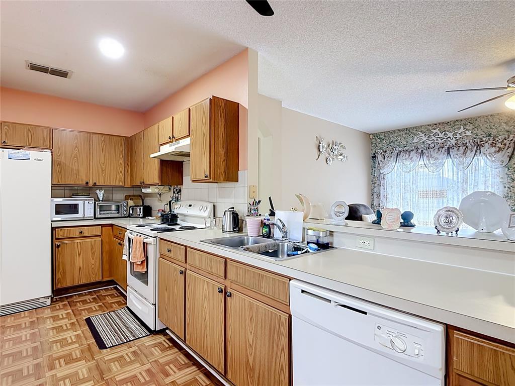 A kitchen with wood cabinets, white appliances, and a pass-through counter overlooking a dining area — 1014 DEDDINGTON PLACE, KISSIMMEE, FL