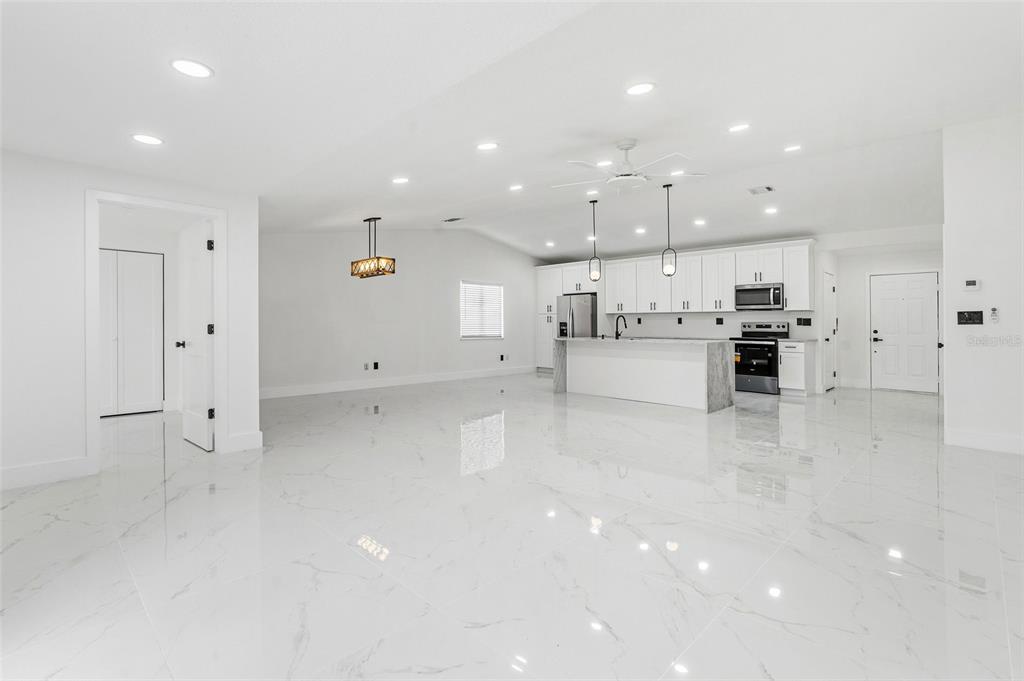 A modern kitchen features white cabinetry, a central island, stainless steel appliances, and marble-look flooring — 5308 BLACK PINE DRIVE, TAMPA, FL