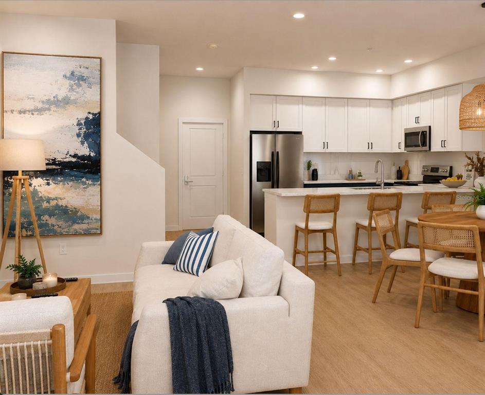 A modern open-concept living room and kitchen with white cabinetry, stainless appliances, and neutral furniture — 134 TESSIE LANE, SANFORD, FL