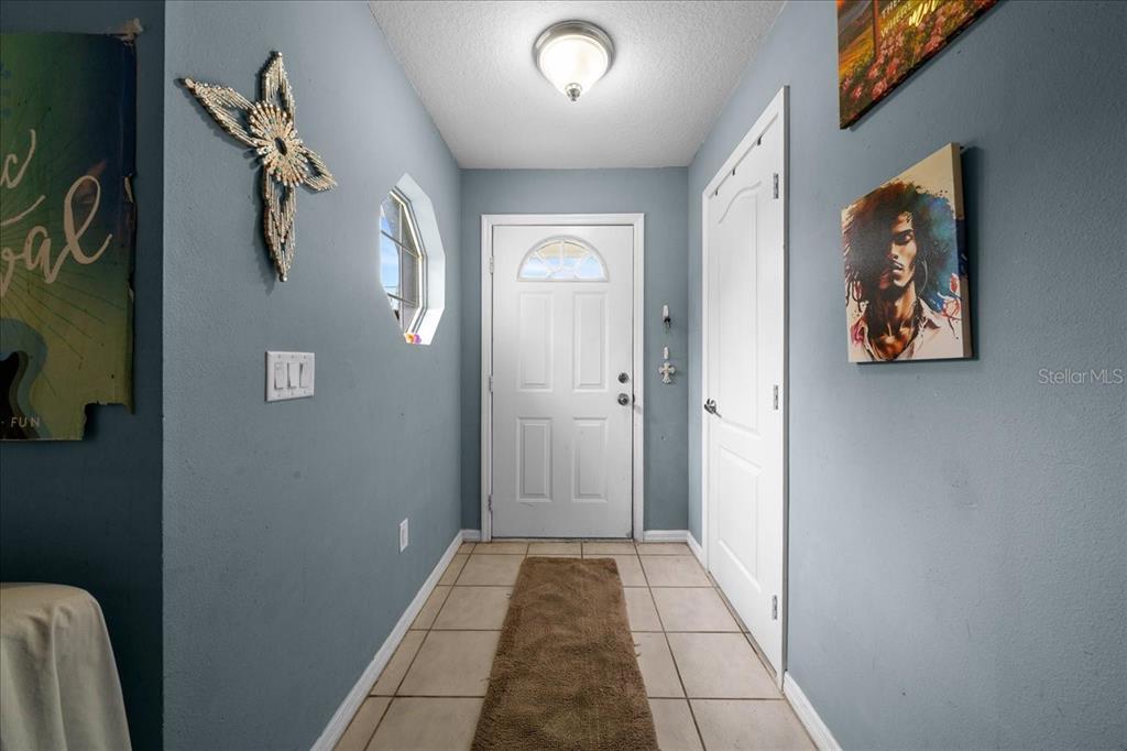 A foyer with light blue walls, tile flooring, a white front door, and wall art — 9 PINE CIRCLE RUN, OCALA, FL