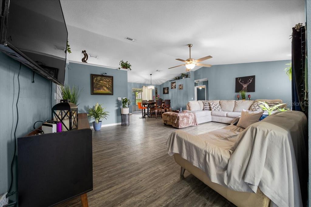 A spacious living room features light blue walls, wood-look flooring, and an open dining area — 9 PINE CIRCLE RUN, OCALA, FL