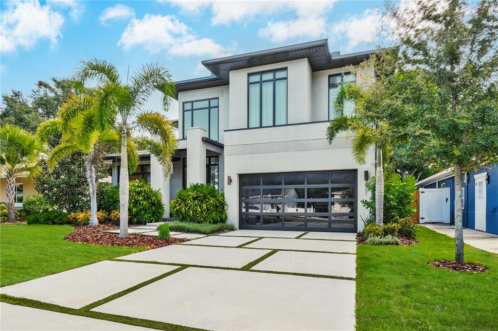 A modern two-story house features a glass garage door, concrete driveway, and palm trees — 1551 PASADENA DRIVE, DUNEDIN, FL