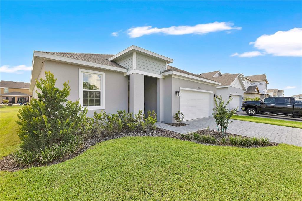 A single-story house with a gray stucco exterior, a two-car garage, and a landscaped lawn. k — 1924 COLUMBUS PATH, ST CLOUD, FL