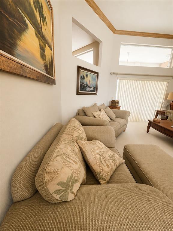 A living room features beige sofas, a patterned ottoman, and wall art under vaulted ceilings — 995 WEATHERSFIELD DRIVE, DUNEDIN, FL