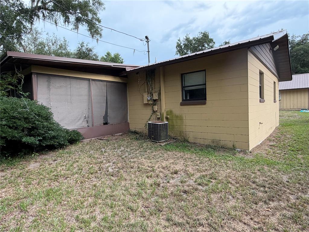 The exterior of a tan concrete block house features a screened porch and HVAC unit — 112 JASPER STREET, BUSHNELL, FL