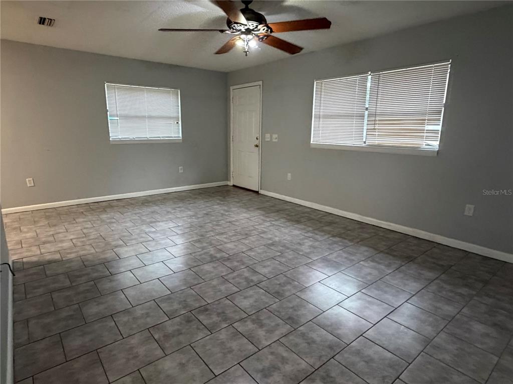 An empty room with gray walls, tile flooring, a ceiling fan, and two windows — 112 JASPER STREET, BUSHNELL, FL