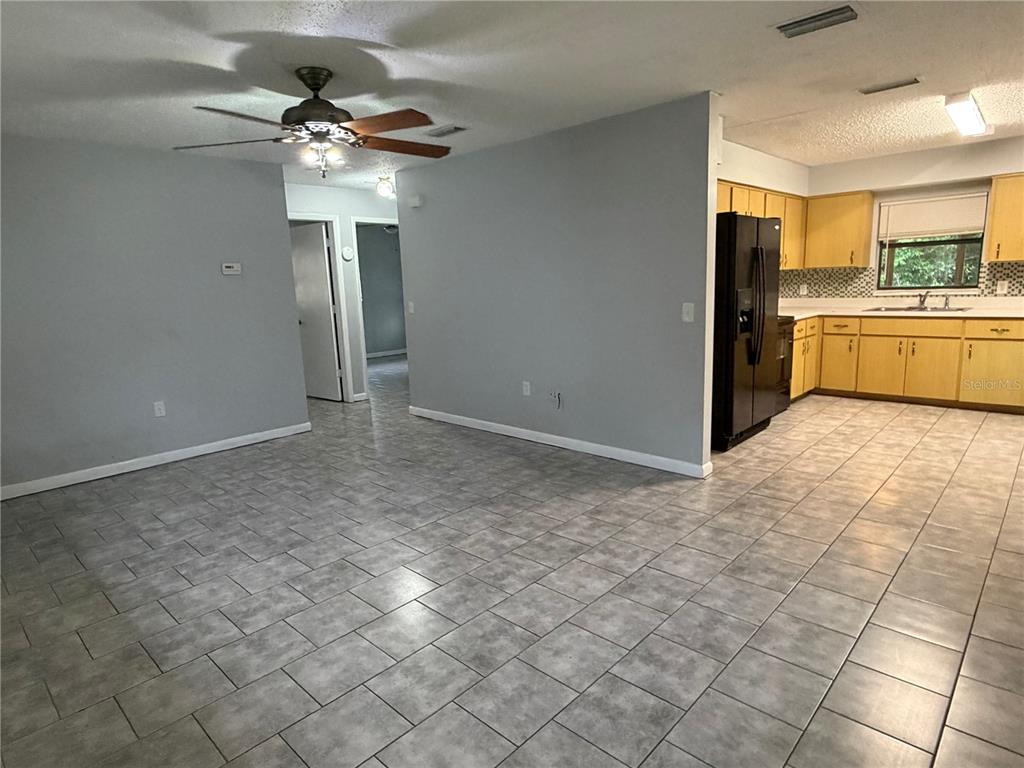 A tiled living area opens into a kitchen with wooden cabinets and black appliances — 112 JASPER STREET, BUSHNELL, FL